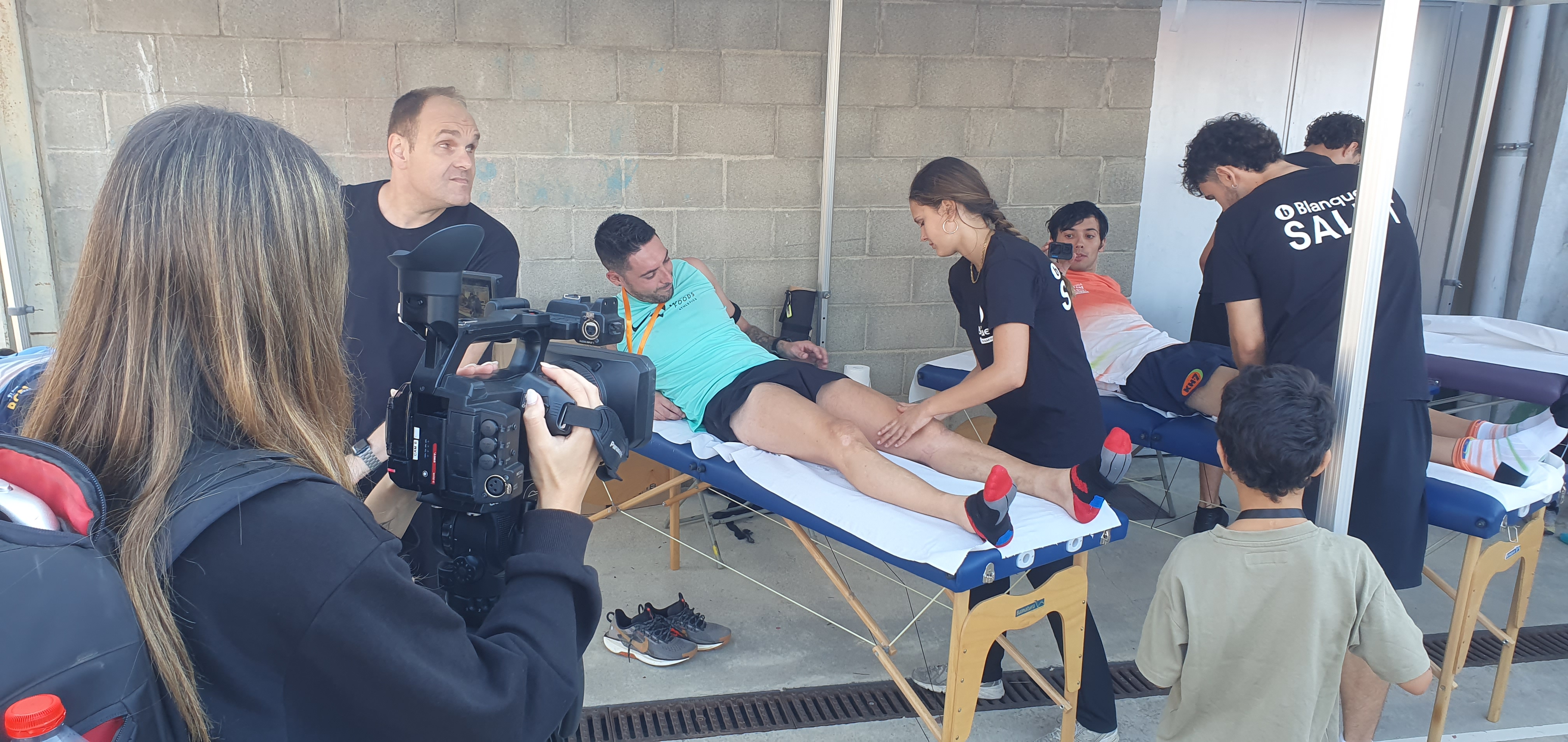 L'alumnat voluntari de donar servei de Fisioteràpia a la cursa. A la imatge també es veu una persona d'esquenes amb una càmera de vídeo, i un dels atletes que està essent tractat també té una càmera, però petita, 360.