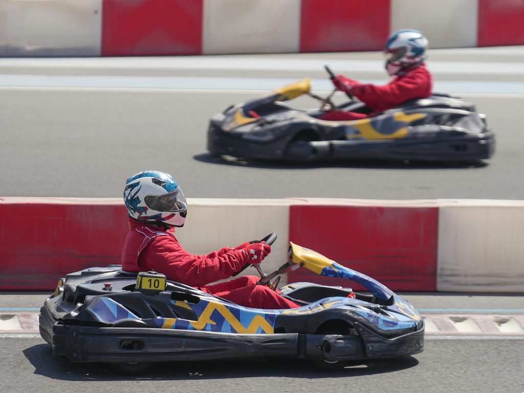 dos persones en cotxes de karting, el que es troba més al davant va cap a la dreta, l'altre a l'esquerra