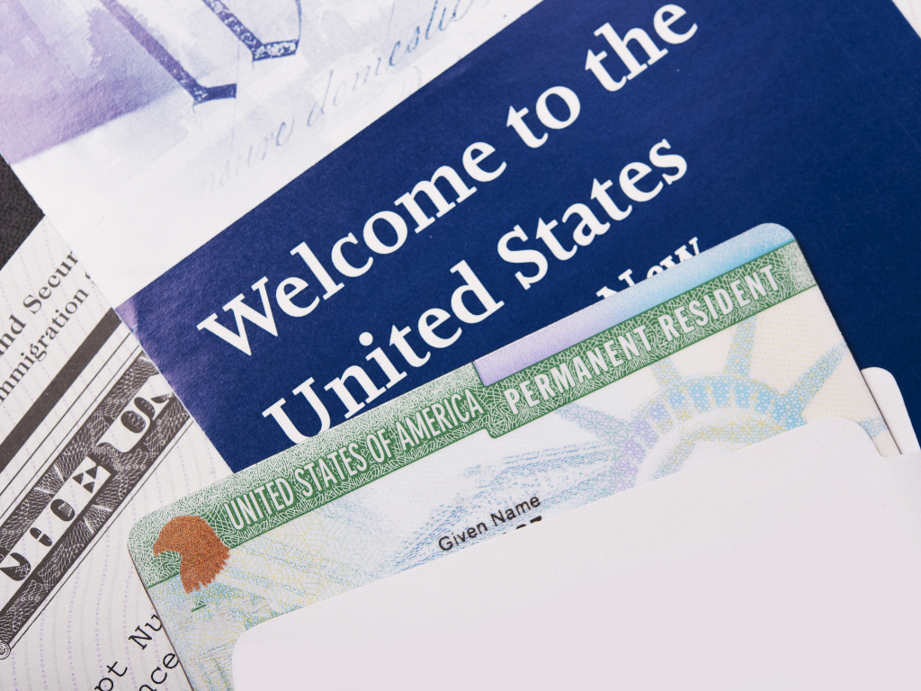 Imatge on veiem molts documents. Primer, un tros d'un passaport de resident d'EUA, i al darrere es veu un paper blau on posa "Welcome to the United States"