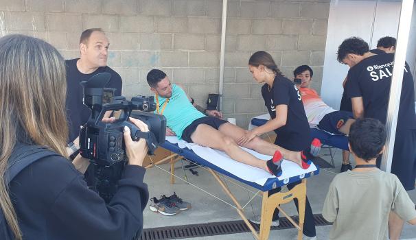 L'alumnat voluntari de donar servei de Fisioteràpia a la cursa. A la imatge també es veu una persona d'esquenes amb una càmera de vídeo, i un dels atletes que està essent tractat també té una càmera, però petita, 360.