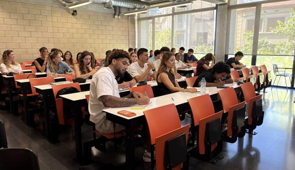 L'alumnat a l'aula durant els cursos de català. La majoria d'estudiants estan concentrats, però hi ha una noia al fons que està mirant a càmera amb el somriure més gran que te pots imaginar
